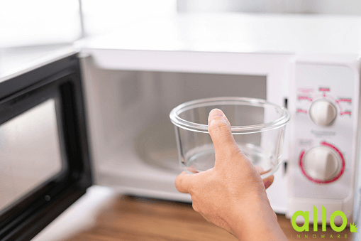 A person holding glass bowl next to microwave oven